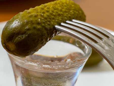 pickled cucumber on a fork on a glass of vodkaの写真素材