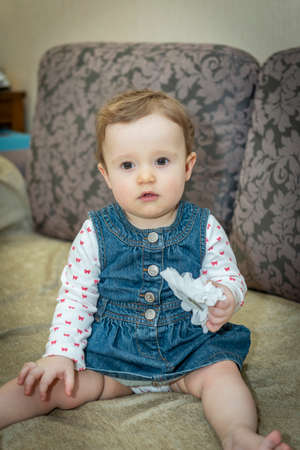 little baby girl in a denim dress on the couchの写真素材