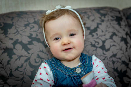 little baby girl in a denim dress on the couchの写真素材