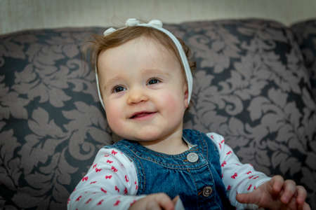 little baby girl in a denim dress on the couchの写真素材