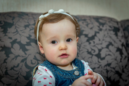 little baby girl in a denim dress on the couchの写真素材