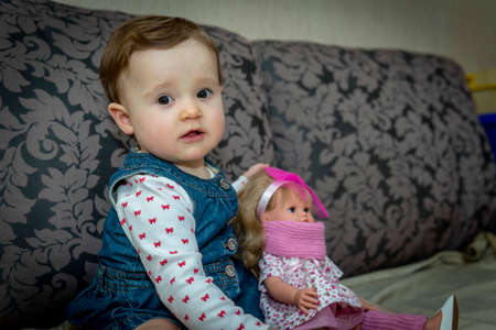 little baby girl with doll on the couchの写真素材