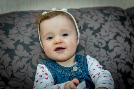 little baby girl in a denim dress on the couchの写真素材