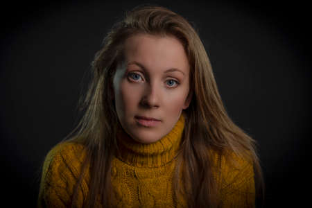 portrait of a young woman in a yellow sweater on a black backgroundの写真素材