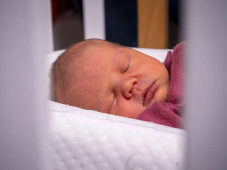 a little newborn baby girl is sleeping in a cribの写真素材