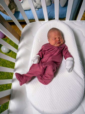 a little newborn baby girl is sleeping in a cribの写真素材