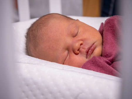 a little newborn baby girl is sleeping in a cribの写真素材