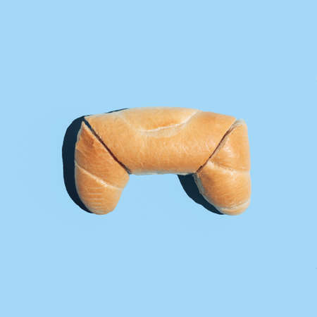 Minimalistic creative flat lay idea with a game controller made of bread on blue background....