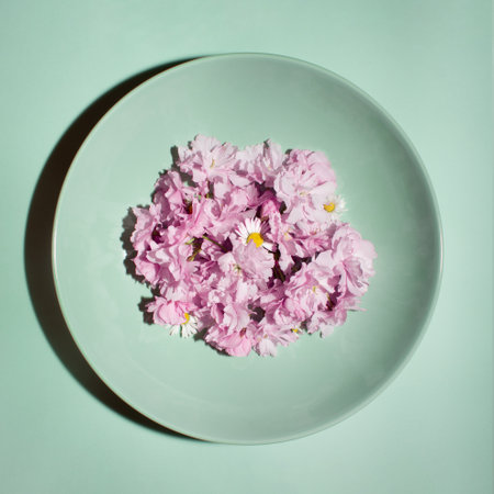 Minimalistic arrangement of a mint colored plate with bright blossoming pink flowers on a pastel background. Retro flat lay concept, stylish creative idea.の写真素材