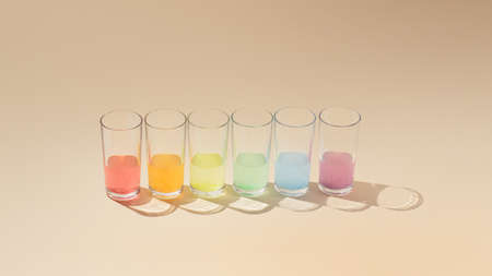 Creative minimalistic idea with colorful liquid in drinking glasses. Rainbow color concept, modern light and shadow concept on pastel beige background. Linear composition.の写真素材