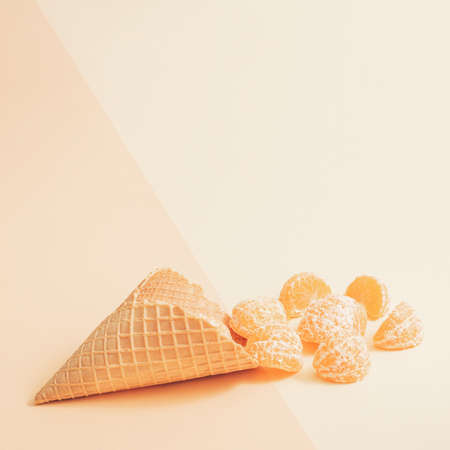 Minimal retro summer concept with an ice cream cone and fresh raw mandarin orange slices. Modern sunny fruit concept, pastel beige colored background.の写真素材