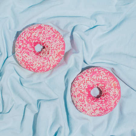 Minimalistic summer vibes concept with pink donuts on bright blue fabric. Creative water and summer vacation idea, square flat lay arrangement.の写真素材
