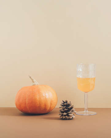 Retro style aesthetic concept with a pumpkin, pine and drinking glass on pastel brown background. Creative 2021 Halloween and autumn idea, minimalistic vertical arrangement.の写真素材