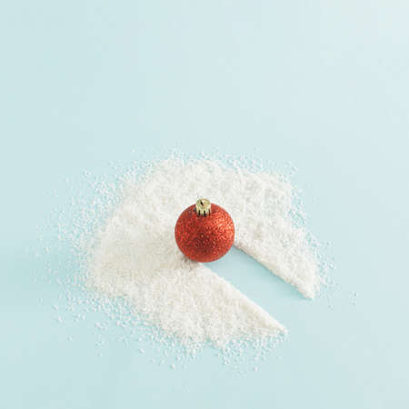 Winter decoration concept with red bauble and snow on bright blue background. Creative Christmas and New Year decoration idea, minimal aesthetic arrangement.の写真素材