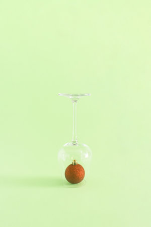 Christmas and New Year decoration idea with a drinking glass and red bauble on pastel bright green background. Creative holiday party and winter concept, minimal vertical aesthetic composition.の写真素材