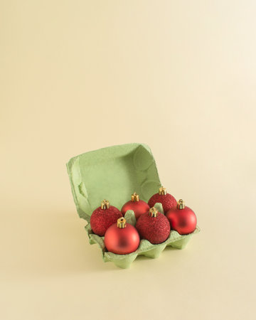Christmas and New Year decoration idea with egg package and red baubles on pastel beige background....