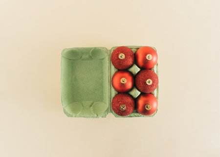 Christmas decoration idea with red baubles in egg package on pastel beige background. Minimal flat lay composition, creative New Year season concept.の写真素材