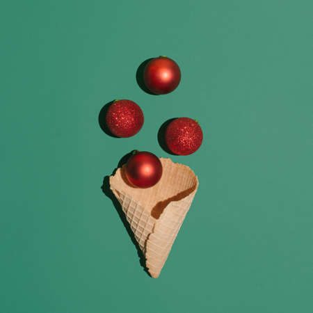 Christmas dÃ©cor and New Year season idea with red baubles and ice cream cone on dark green background. Creative surreal concept, minimal flat lay composition.の写真素材