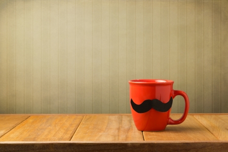 Red cup with paper mustache on wooden table over retro wallpaperの写真素材