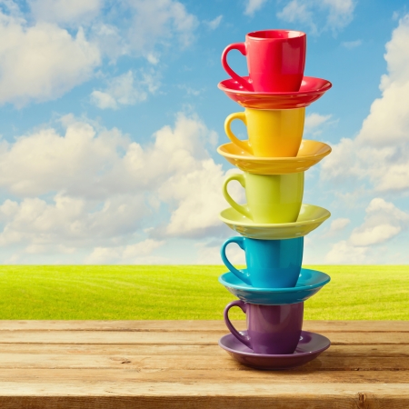 Rainbow color cups on wooden table over beautiful sky and meadow.の写真素材