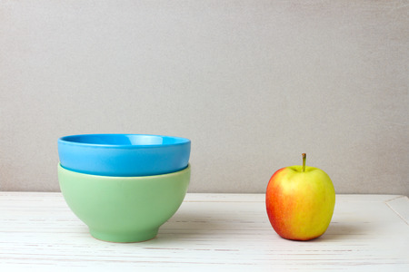 Two colorful bowls and apple on white wooden table and grey grunge backgroundの写真素材