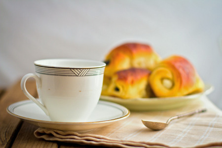White cup and fresh buns on plate on wooden tableの写真素材