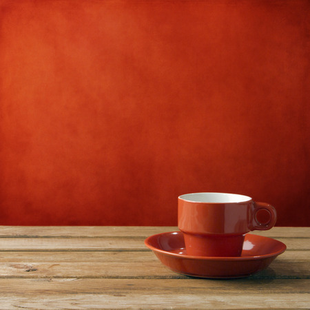 Red coffee cup on wooden deck tabletop against red grunge wallの写真素材