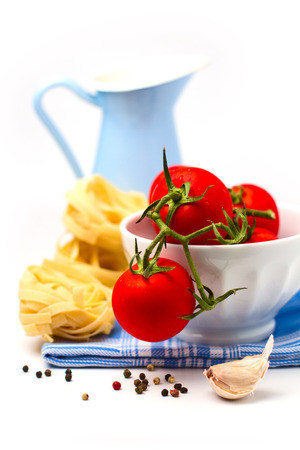 Tomatoes in white bowl and pasta arranged on white backgroundの写真素材