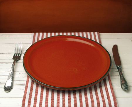 Empty red ceramic plate on white table against red grunge wallの写真素材