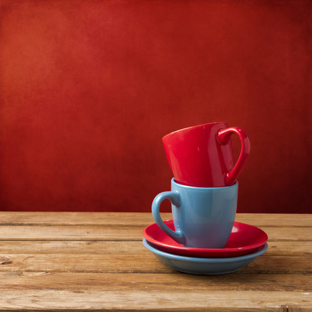 Red and blue coffee cups on wooden table over red grunge wallの写真素材