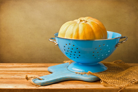 Pumpkin in blue colander on wooden tabletop against grunge wallの写真素材