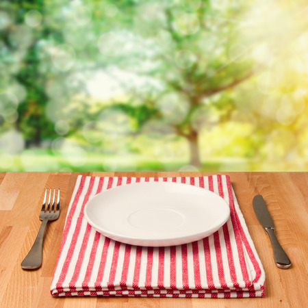 Empty plate with silverware on wooden table over bokeh backgroundの写真素材