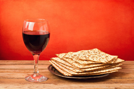 Glass of red wine and matza on wooden table over grunge red backgroundの写真素材
