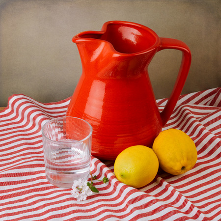 Still life with red jug and lemons on red striped tableclothの写真素材