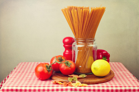 Whole wheat spaghetti and vegetables on red tablecloth. Still life composition.の写真素材