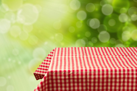 Empty table with red checked tablecloth over green bokeh backgroundの写真素材