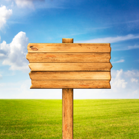 Wooden sign over beautiful green meadow and blue skyの写真素材