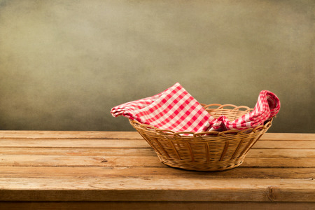Empty basket with checked tablecloth on wooden table over grunge backgroundの写真素材