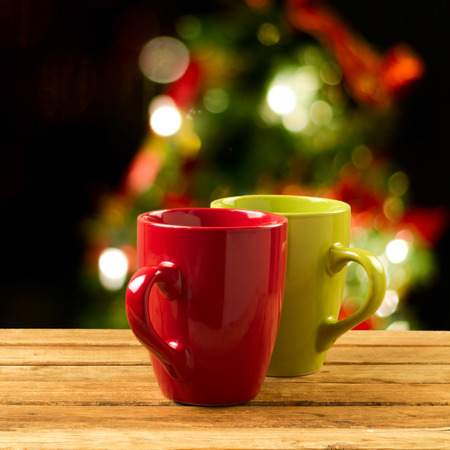 Christmas holiday mugs on wooden table over Christmas tree bokeh backgroundの写真素材