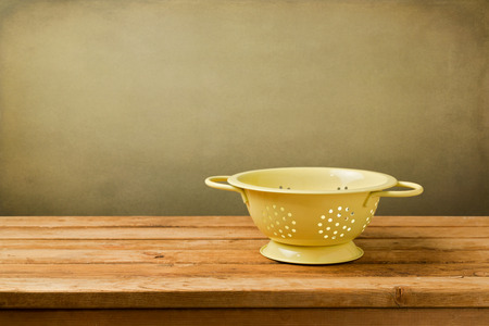 Empty colander on wooden deck table over grunge backgroundの写真素材