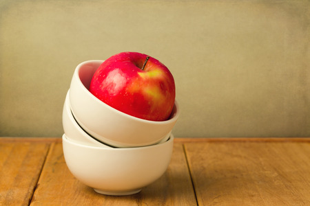 Red apple in stack of bowls on wooden table over grunge backgroundの写真素材