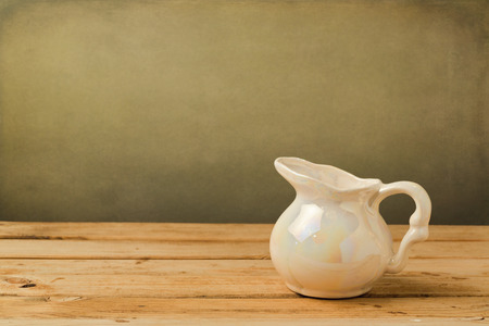 Vintage milk pitcher on wooden deck table over grunge backgroundの写真素材