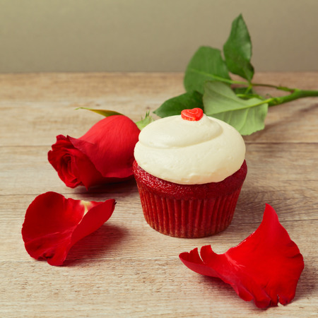 Valentine's day cupcake with red roses and petals on wooden tableの写真素材