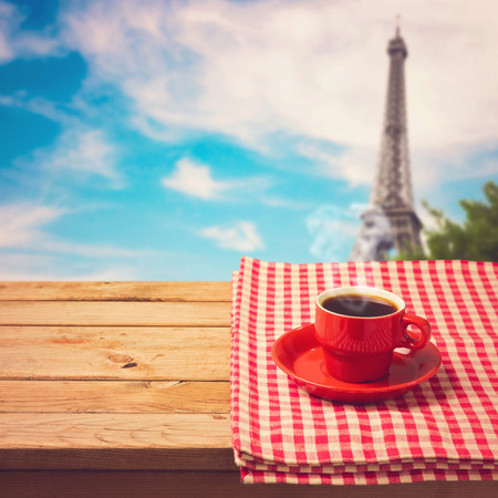 Coffee cup with checked tablecloth on wooden table over Eiffel tower in Paris, Franceの写真素材