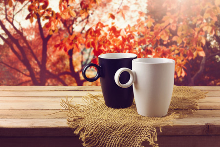 White and black cup with beverage on wooden table over beautiful nature backgroundの写真素材