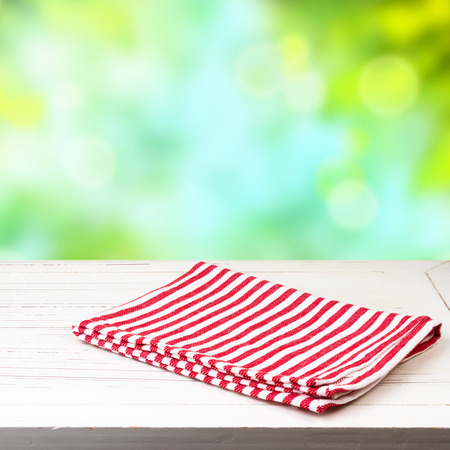 Empty white wooden table and red striped tablecloth over nature bokeh backgroundの写真素材