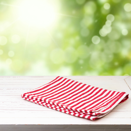 Background with white wooden table and red striped tablecloth over green bokehの写真素材