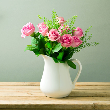 Rose flower bouquet in white jug on wooden tableの写真素材