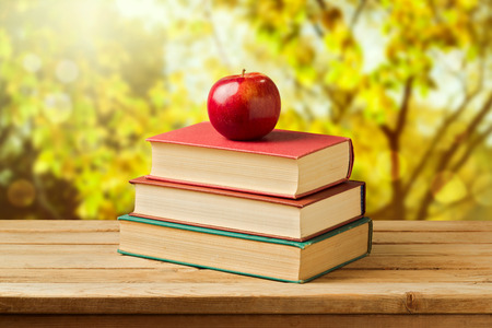 Back to school concept. Apple on old books over autumn trees backgroundの写真素材