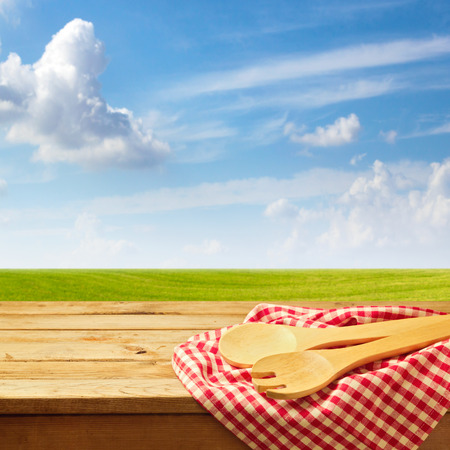 Wooden table with kitchen utensil over green meadow and blue skyの写真素材